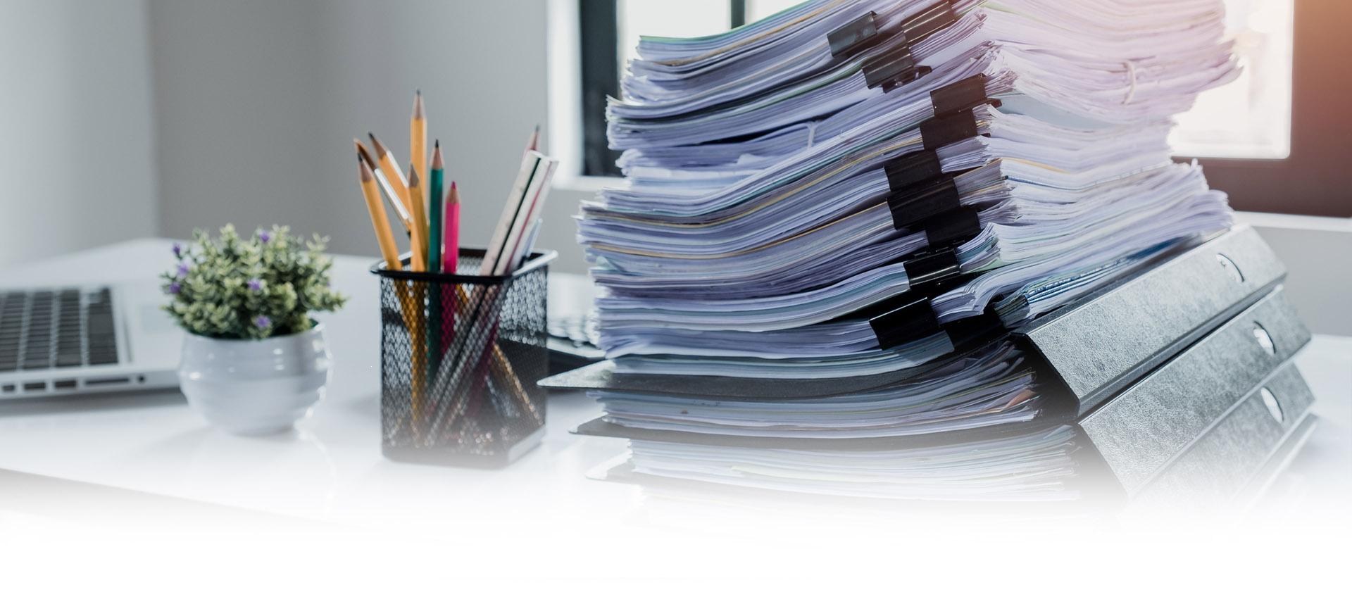 Stos dokumentów na biurku na którym znajduje się również organizer z ołówkami Slajd 2